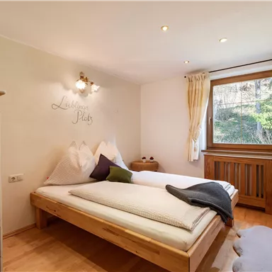 Ein einfaches Schlafzimmer mit einem großen Bett und Holzfußboden. Es gibt Fenster mit Blick ins Grüne und eine gemütliche Einrichtung.