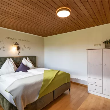 Ein gemütliches Schlafzimmer mit einem großen Bett und einer modernen Holzwand. Neben dem Bett steht ein weißer Schrank und eine dekorative Wanduhr.