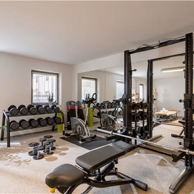 A modern gym with weights and exercise equipment. The room is bright and well-equipped, ideal for training at home.