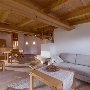 A cozy living area with wooden beams and a light sofa. In the background, a dining area is visible, which looks inviting.
