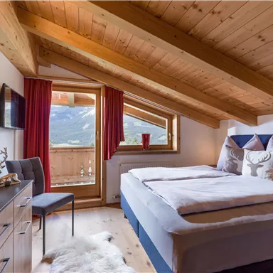 A cozy bedroom with wooden-paneled ceiling and large windows. The room is bright and furnished in a modern style, with a beautiful view of the mountains.