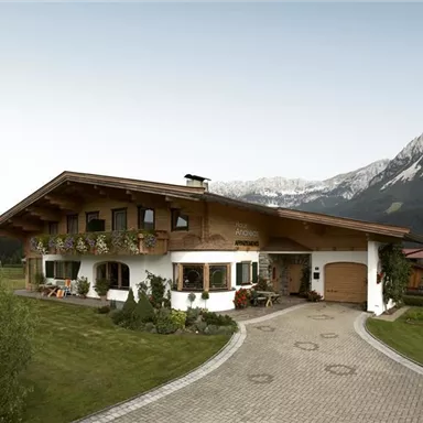 A beautiful Alpine house with flower-filled balconies. Majestic mountains can be seen in the background.