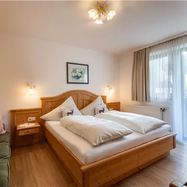 A cozy bedroom with wooden furniture and a double bed. Large windows let in plenty of daylight and create a bright atmosphere.