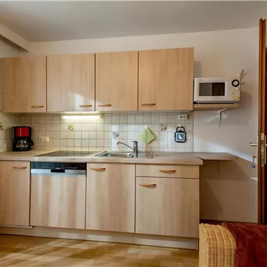 A modern kitchen with light wood cabinets and a microwave. On the countertop, a kettle and a coffee machine can be seen.