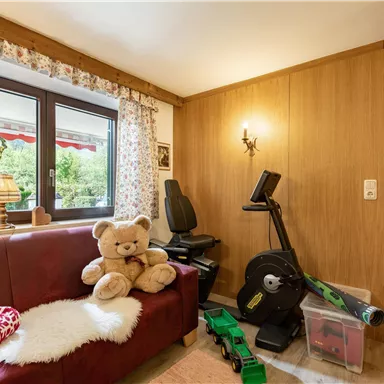 A cozy room with a red sofa and a large stuffed animal. In the background, there is a fitness equipment and decorative curtains.