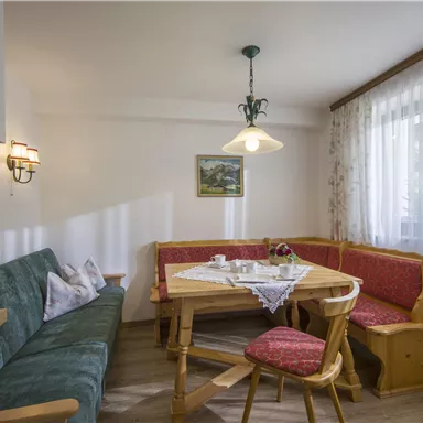 A cozy kitchen with a round table and a corner bench. The room is bright and cheerful with a window and soft lighting.