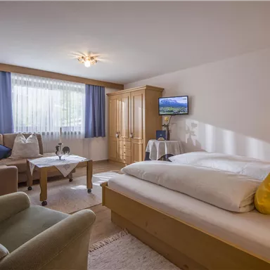 A cozy room with a large bed and a sitting couch. Bright colors and plenty of daylight create an inviting atmosphere.