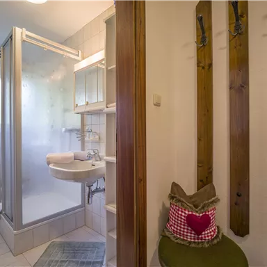 A modern bathroom with a shower, a sink, and wooden shelves. The decor is bright and friendly.
