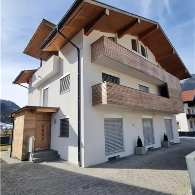 Ein modernes Haus mit Holzverkleidungen und Balkonen. Der klare Himmel und die Umgebung verleihen dem Gebäude ein einladendes Ambiente.