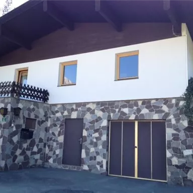 A modern house with a stone facade and a wood overhang. The windows are framed in yellow and the surroundings appear well-maintained.