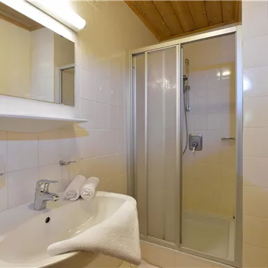 Ein modernes Badezimmer mit einer Dusche und einem Waschbecken. Helle Fliesen und Holzdetails schaffen eine einladende Atmosphäre.