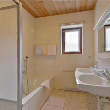 Ein helles Badezimmer mit Dusche und Badewanne. Weiße Fliesen und ein Fenster sorgen für eine freundliche Atmosphäre.