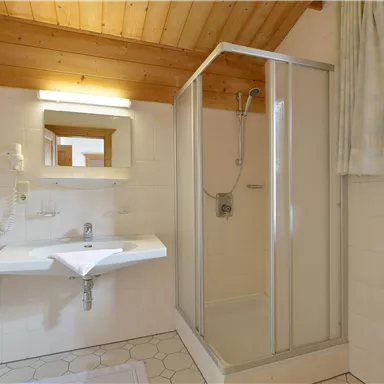 Ein modernes Badezimmer mit einer Dusche und einem Waschbecken. Die Holzdecke sorgt für eine gemütliche Atmosphäre.