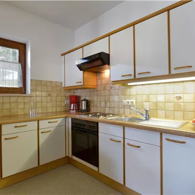 Eine moderne Küche mit weißen Schränken und Holzdetails. Es gibt eine Mikrowelle, einen Herd und eine Obstschale auf der Arbeitsplatte.