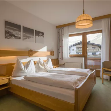 Ein gemütliches Schlafzimmer mit zwei Einzelbetten und Holzmöbeln. Ein großes Fenster bietet einen Blick auf die Berge.