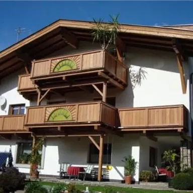 A two-story house with wooden cladding and balconies. The garden is well-maintained and has plants as well as seating areas.