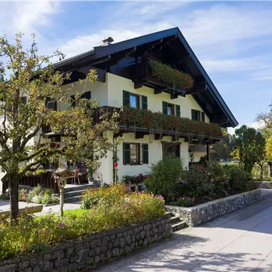 Ein traditionelles Haus mit Holzbalcon und bunten Blumenkästen. Die Umgebung ist grün und einladend, ideal für einen ruhigen Tag im Freien.