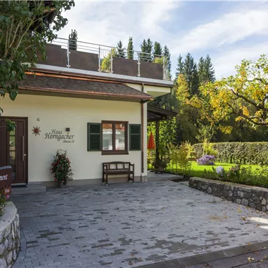 Ein charmantes Haus mit einem gepflegten Garten und begrünten Bäumen. Der Eingangsbereich ist einladend und freundlich gestaltet.