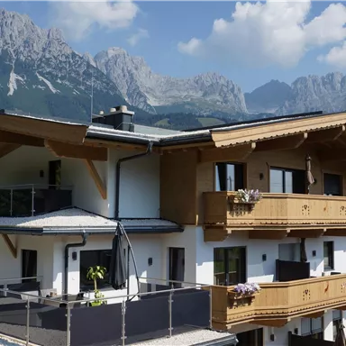 Ein modernes Haus mit Holzverkleidung vor einer beeindruckenden Berglandschaft. Der Himmel ist klar und die Atmosphäre ist einladend.