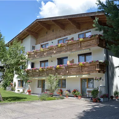 A charming building with balconies, surrounded by trees and flowers. The sky is clear and blue, creating an inviting atmosphere.