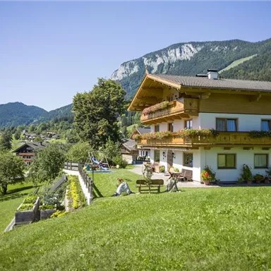 Ein malerisches Haus in einer grünen Landschaft, umgeben von Bergen. Der Himmel ist klar und die Umgebung wirkt einladend und ruhig.