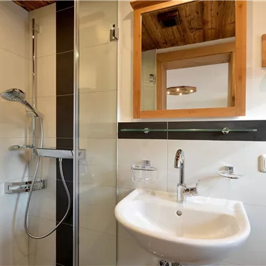 A modern bathroom with a shower and sink. Bright tiles and wooden paneling create a friendly atmosphere.