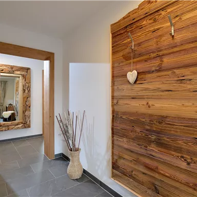 A modern hallway with a wooden wall panel and stylish decorations. A mirror and a vase with dried flowers enhance the cozy atmosphere.