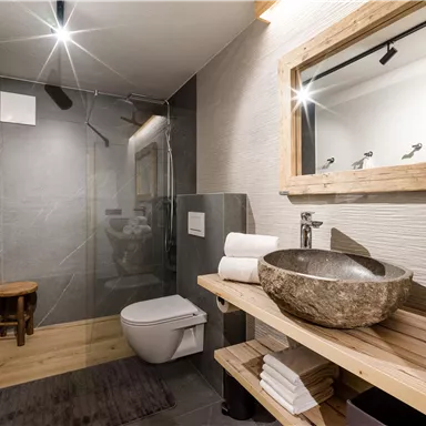 Ein modernes Badezimmer mit einer eleganten Dusche und einem großen Spiegel. Die Holzregale sind mit Handtüchern und einer dekorativen Waschschüssel ausgestattet.