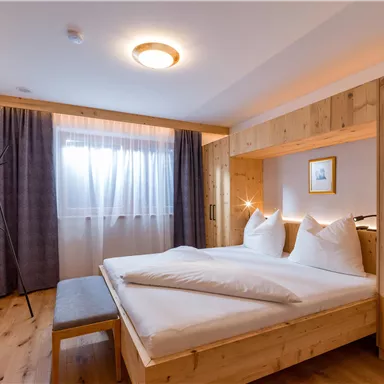 Ein gemütliches Schlafzimmer mit Holzmöbeln und zwei Betten. Bohnenvorhänge lassen viel natürliches Licht herein.