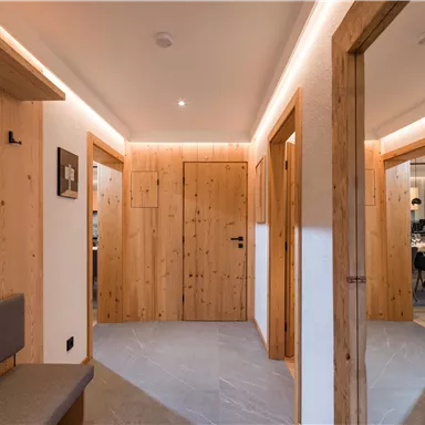 Ein moderner Flur mit Holzvertäfelungen und sanfter Beleuchtung. Die Türen führen zu verschiedenen Räumen und schaffen eine einladende Atmosphäre.