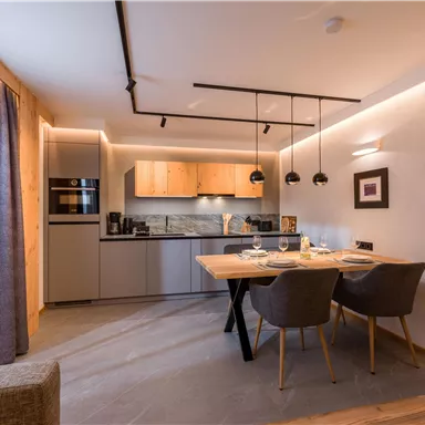 Eine moderne Küche mit einem Essbereich. Der Raum ist hell und einladend, ausgestattet mit grauen Stühlen und Holzdetails.