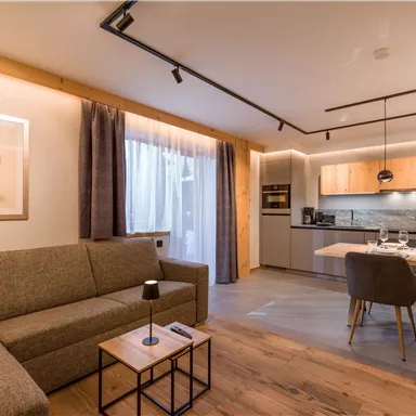 Ein modernes Wohnzimmer mit einer gemütlichen Couch und einem Esstisch. Die Küche ist gut ausgestattet und das Licht ist warm und einladend.