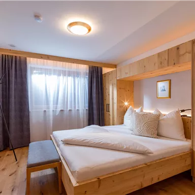 Ein modernes Schlafzimmer mit Holzvertäfelungen und einem gemütlichen Bett. Große Fenster lassen natürliches Licht herein und schaffen eine einladende Atmosphäre.