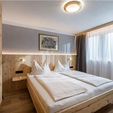 Ein modernes Schlafzimmer mit hellem Holz und einem großen Fenster. Die Bettwäsche ist weiß und die Wände sind sanft grau gestrichen.