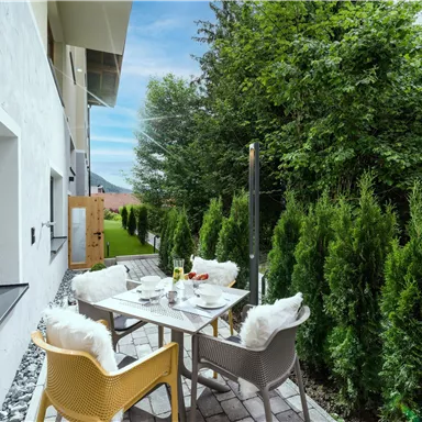 Ein einladender Außenbereich mit einem Tisch und Stühlen, umgeben von grünen Hecken. Der Bereich ist hell und freundlich mit Blick auf den Garten.