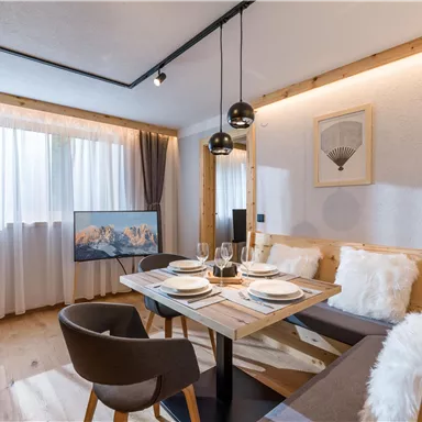 Ein modernes Esszimmer mit einem Holztisch, eleganten Stühlen und wunderschöner Dekoration. Große Fenster lassen viel Licht herein und schaffen eine einladende Atmosphäre.