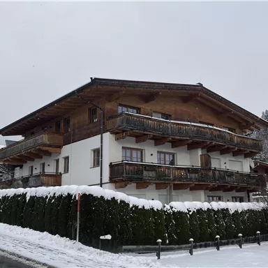 A cozy wooden house in the snow with balconies. In the background, snow-covered trees can be seen.