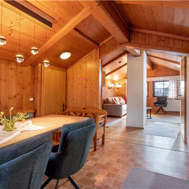 A cozy living area with a wooden ceiling and modern dining area. Plenty of light falls through the windows, creating an inviting atmosphere.