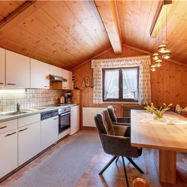 A cozy, modern kitchen with wooden ceilings and a large dining table. The space is brightly lit and offers an inviting place to cook and eat.