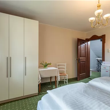 A cozy room with two beds, a wardrobe, and a table. Curtains hang on the wall and the decor is simple and bright.