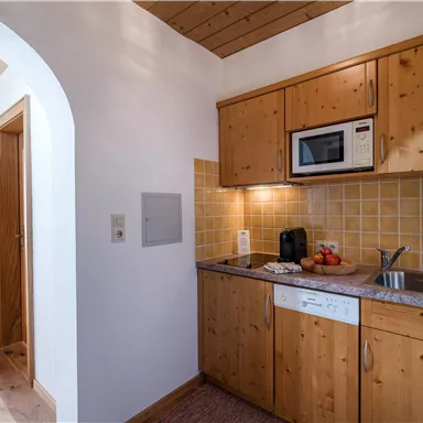A cozy kitchen with wooden furniture and modern appliances. The walls are light, and there is a small workspace with a sink and a microwave oven.