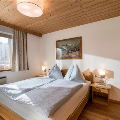 A cozy bedroom with a double bed and wooden paneling. There is a window with curtains and a picture on the wall.
