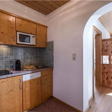 A modern kitchen corner with wooden furniture and a bright, friendly atmosphere. There is a stove, a microwave, and a sink in the kitchen.