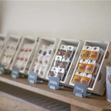 Eine Auswahl an verpackten Süßigkeiten und Honig in ansprechenden Boxen. Neben den Produkten steht ein dekorativer Kerzenhalter.