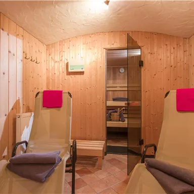 Ein gemütlicher Wellnessbereich mit Holzvertäfelung. Zwei Liegen mit Handtüchern und Sicht auf eine Sauna.