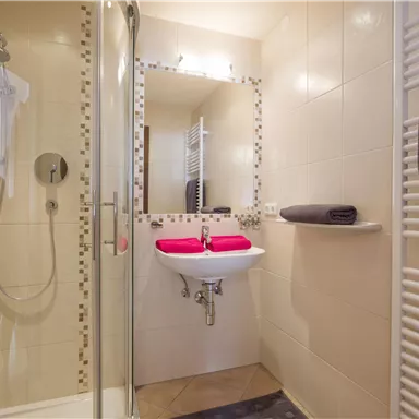 Ein modernes Badezimmer mit einer Dusche und einem Waschbecken. Die Wände sind hell gefliest und es liegen Handtücher bereit.