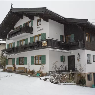 Ein charmantes Haus im alpinen Stil, umgeben von Schnee. Die Fensterläden sind in einem grünen Farbton gehalten und verleihen dem Gebäude eine gemütliche Atmosphäre.