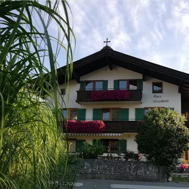 Ein traditionelles Haus mit einem Holzdach und bunten Blumen auf den Balkonen. Die umgebende Vegetation verleiht dem Bild eine einladende Atmosphäre.
