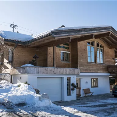 A traditional wooden cottage in the snow. The surrounding area is wintry with a clear blue sky.
