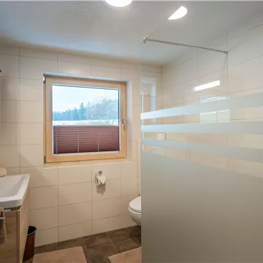 Ein modernes Badezimmer mit Dusche und Waschbecken. Große Fenster sorgen für viel natürliches Licht.